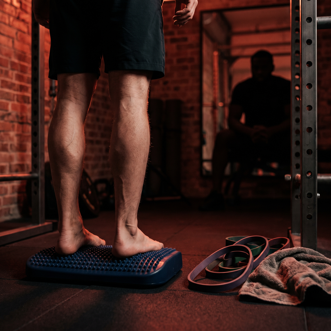 Person standing barefoot on blue foot massage board in home gym for post-workout foot recovery