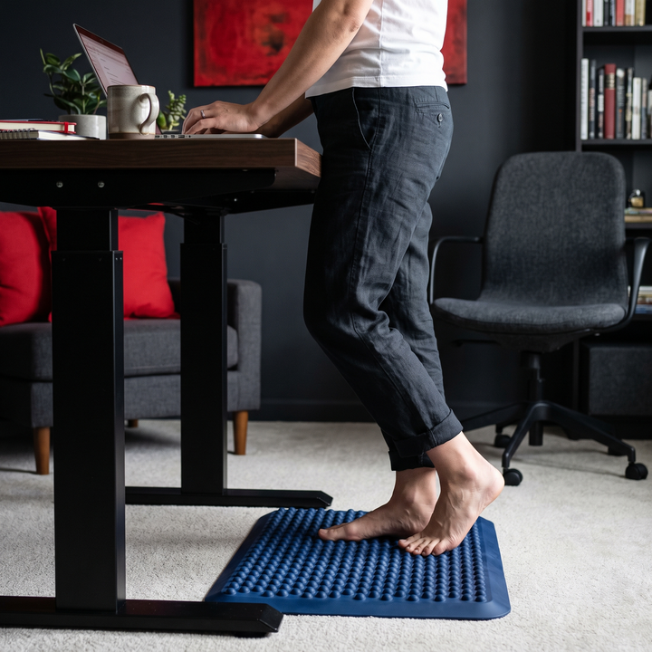 Person using blue foot massage board at a standing desk for foot comfort