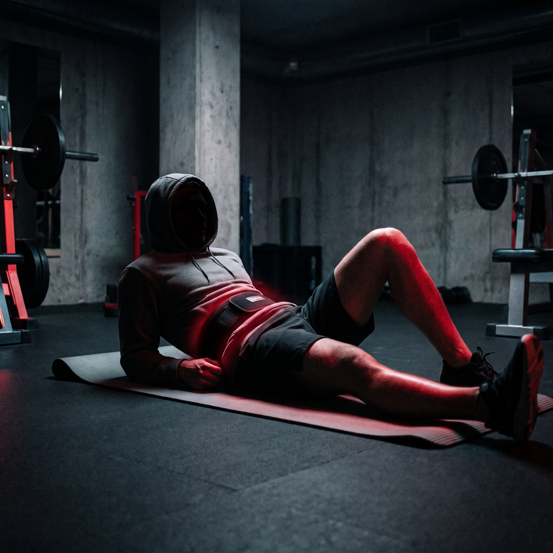 Person lying down wearing a cordless waist recovery belt glowing with red light during a relaxation routine