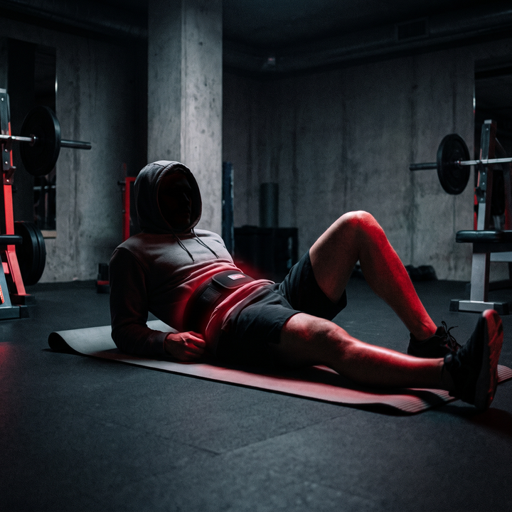 Person lying down wearing a cordless waist recovery belt glowing with red light during a relaxation routine