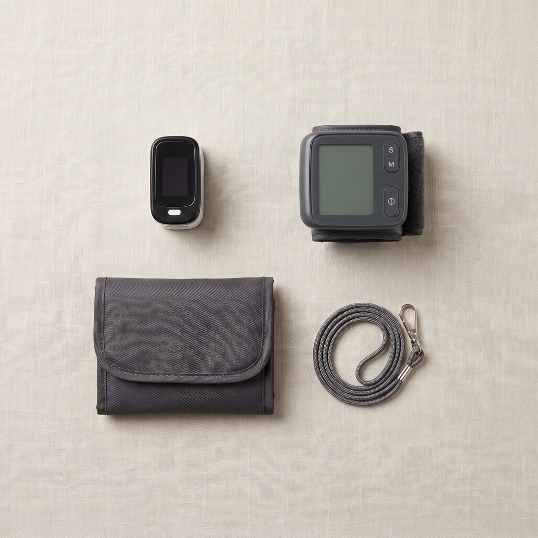 Home health monitoring kit flat lay featuring a finger pulse oximeter, wrist blood pressure monitor, and carrying pouch