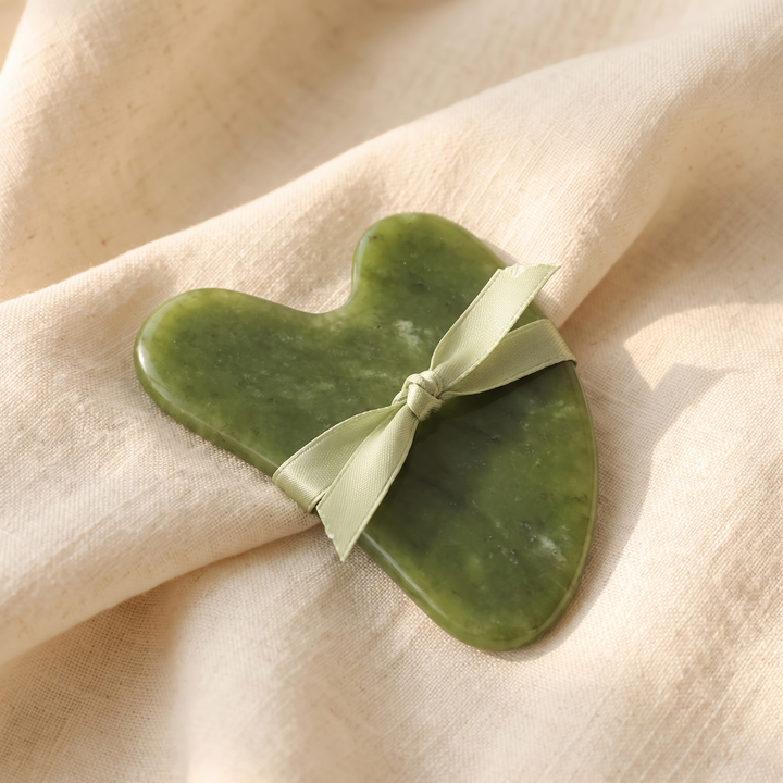 Heart-shaped jade gua sha tool presented as an elegant gift with ribbon
