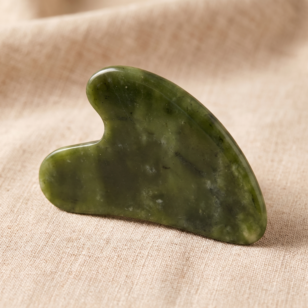 Heart-shaped jade gua sha massage tool shown at an angle on linen