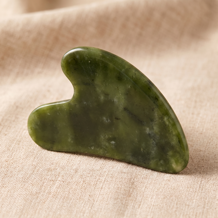 Heart-shaped jade gua sha massage tool shown at an angle on linen