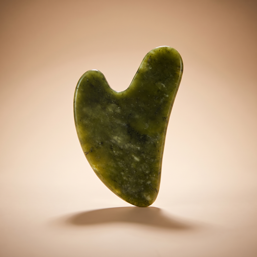 Heart-shaped jade gua sha tool standing upright with warm rim lighting