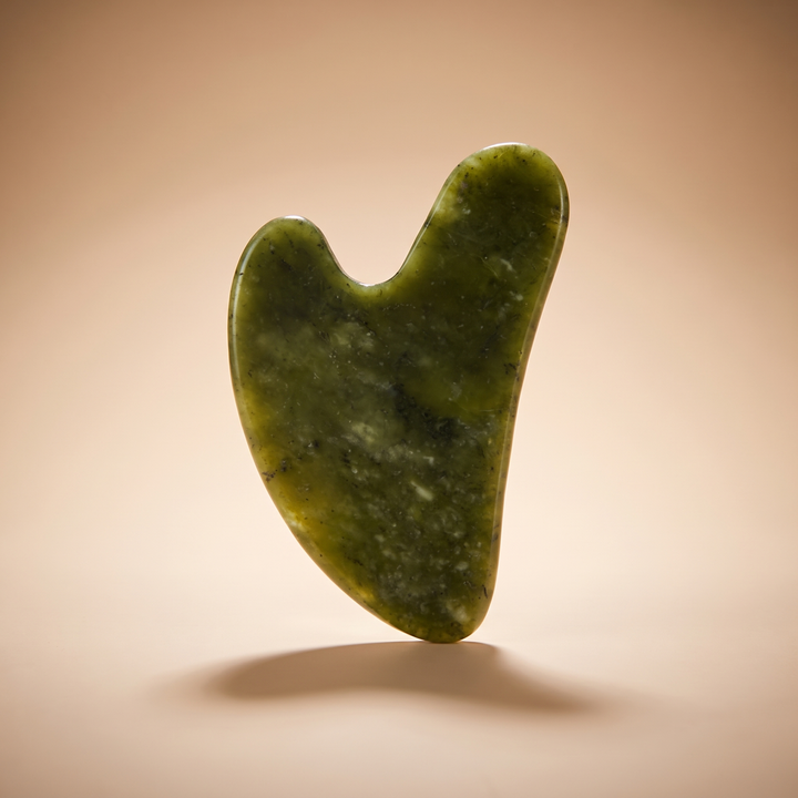 Heart-shaped jade gua sha tool standing upright with warm rim lighting