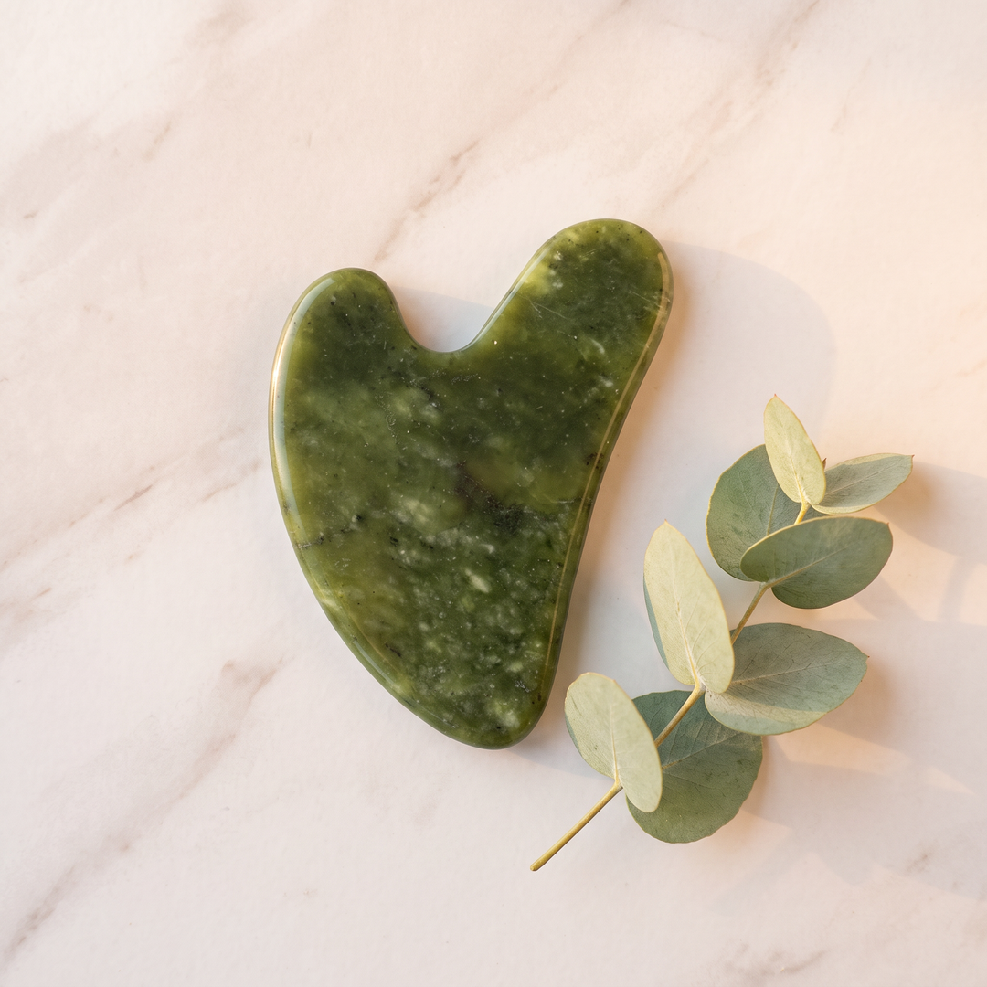 Top-down view of heart-shaped jade gua sha beauty tool on marble surface