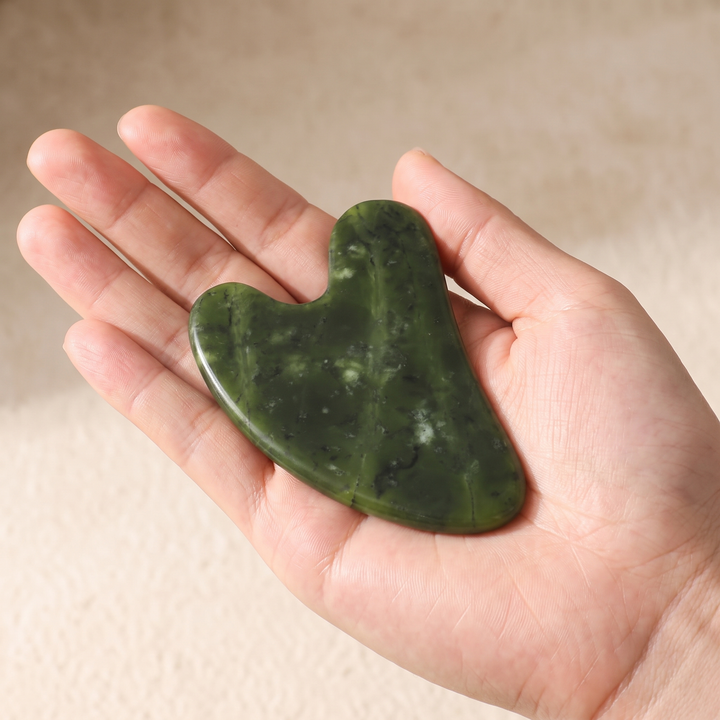 Jade gua sha tool resting in a palm to show compact size