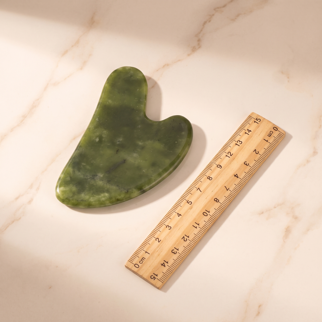 Jade gua sha tool next to a ruler showing size dimensions