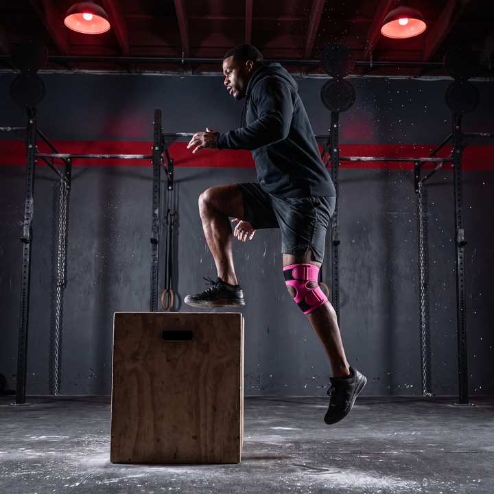 Athlete wearing pink knee support strap during explosive box jump training