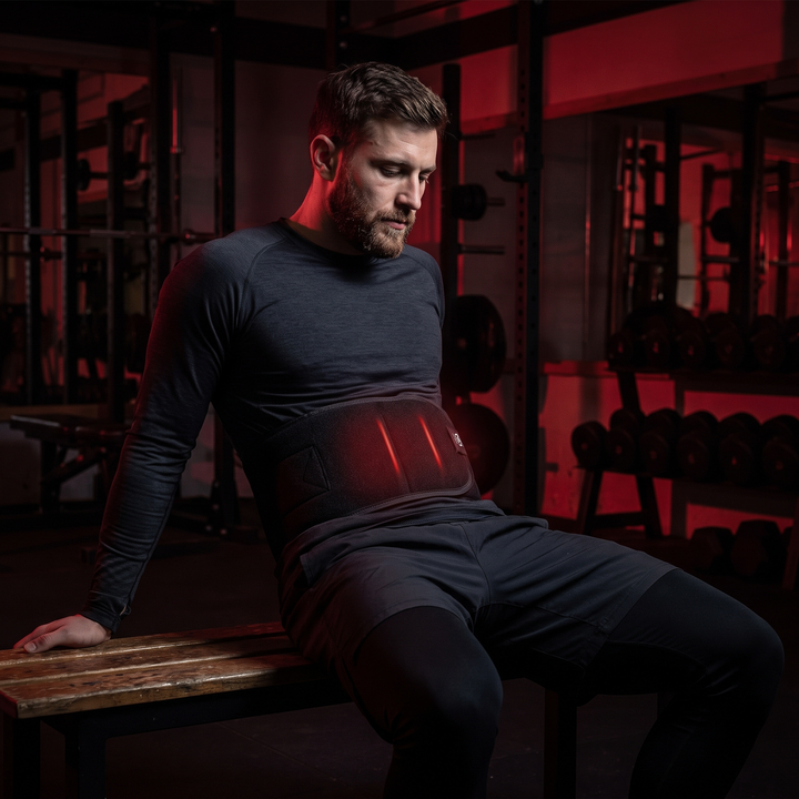 Athlete wearing black LED heat wrap around waist during a recovery session in a dark gym