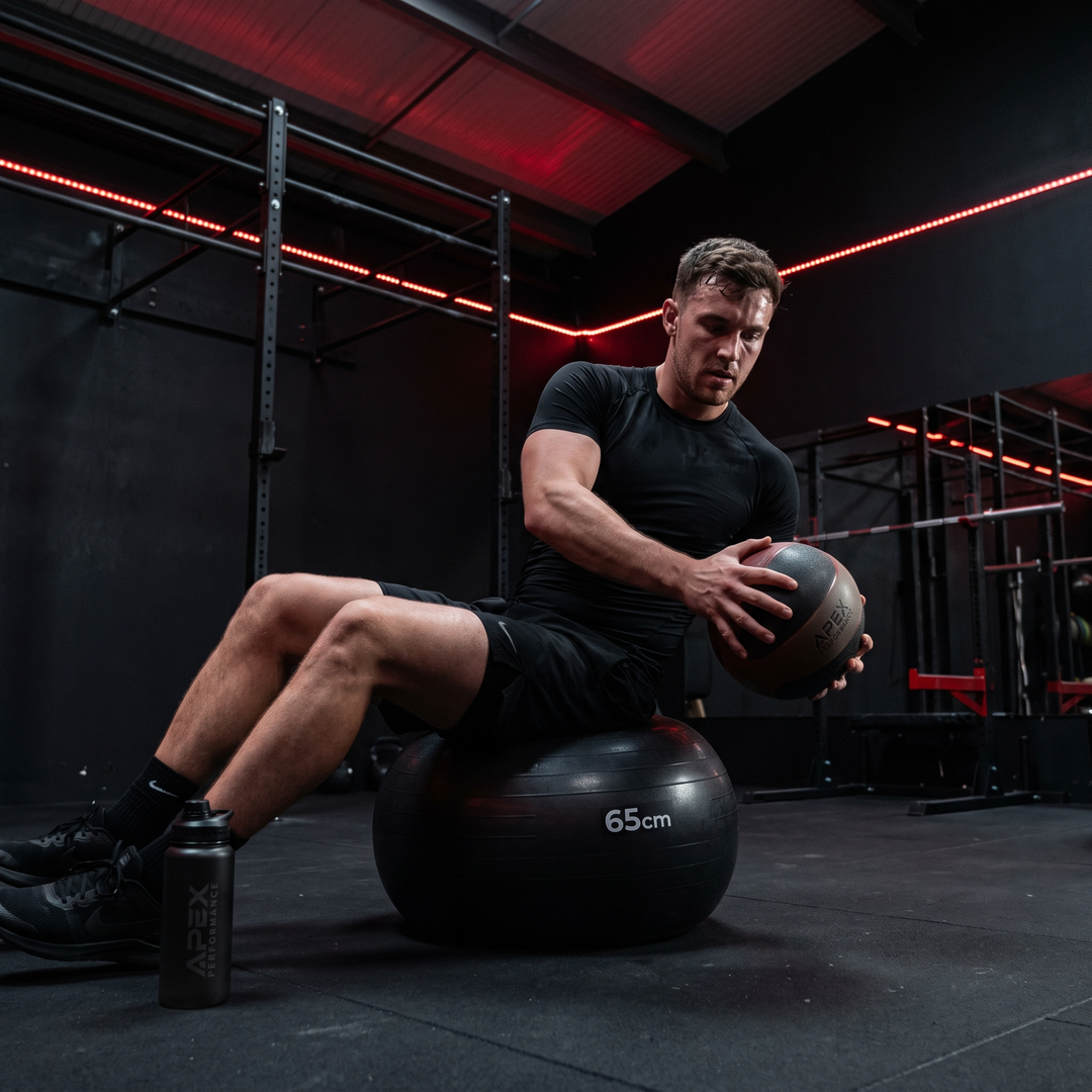 Athlete performing seated core stability exercise on stability ball in dark gym