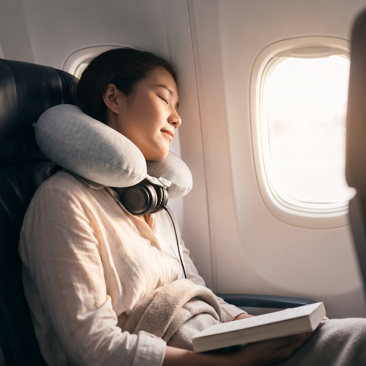Traveler resting comfortably with a light grey travel neck pillow on an airplane