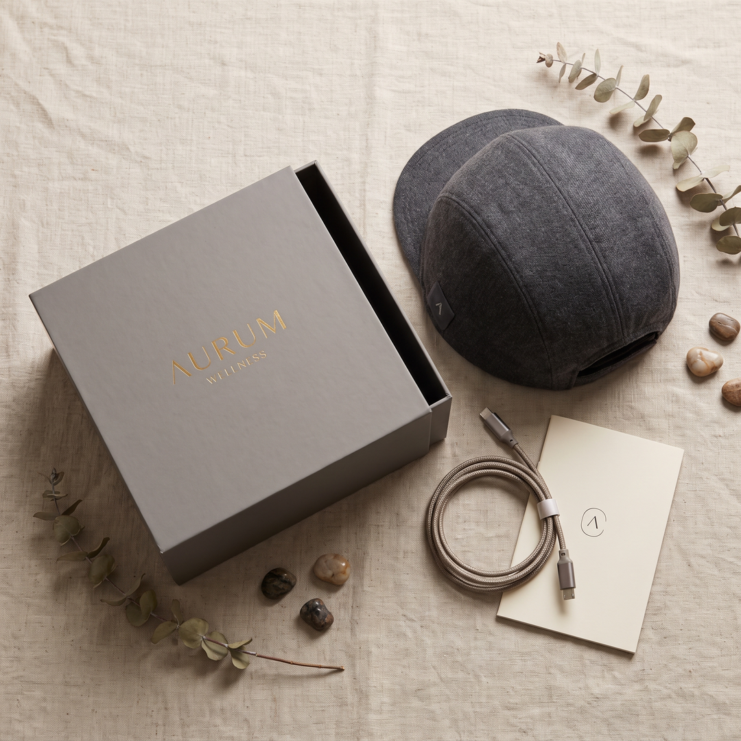 Flat lay of the grey scalp care cap with retail packaging box, charging cable and instruction booklet
